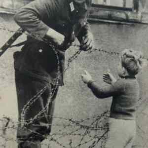 Obrázek 'An East German soldier helps a boy over the barbed wire on the East-West border'